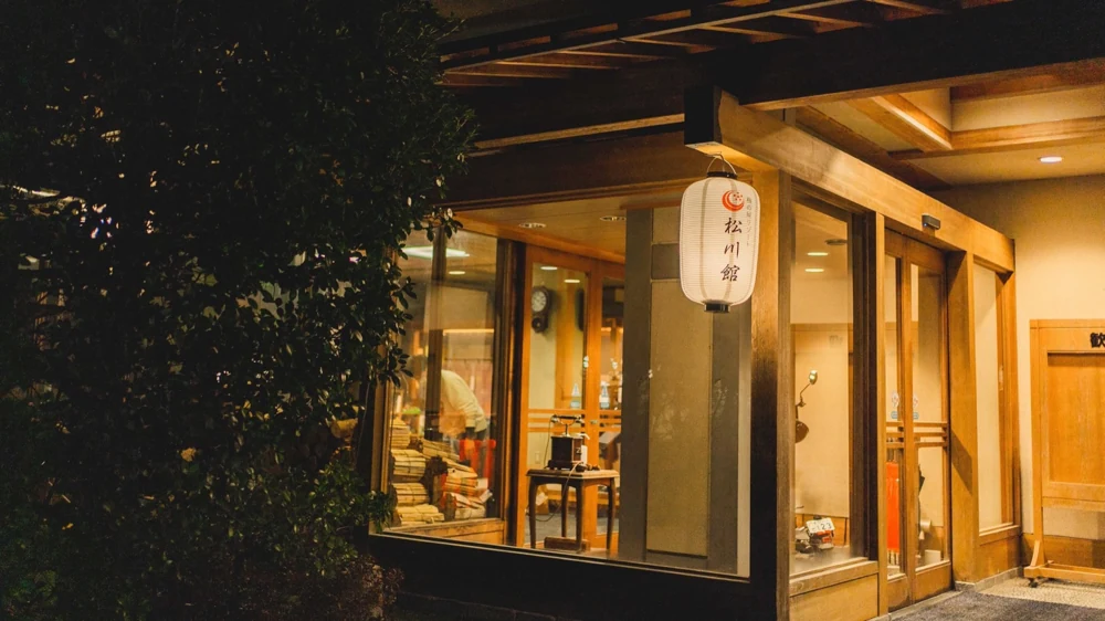 松川館の玄関。木の扉と松川館の提灯が温かい光に照らされている。